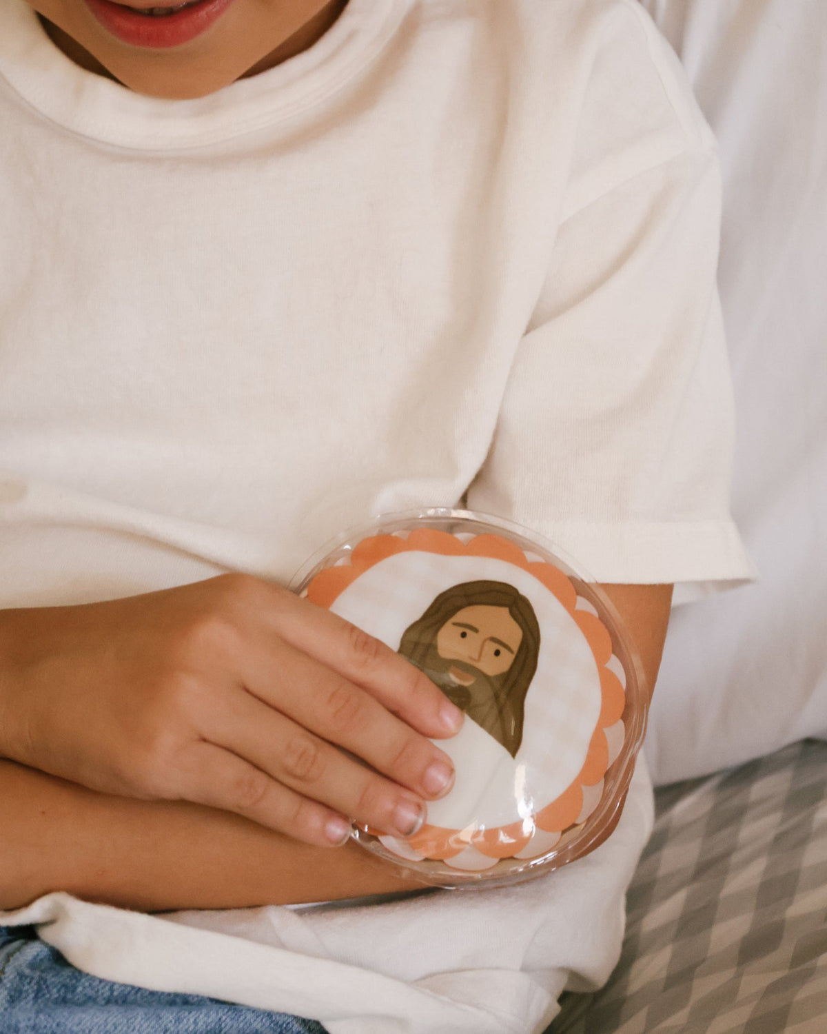 Child resting an orange gingham Jesus Heals hot and cold pack on a tummy ache