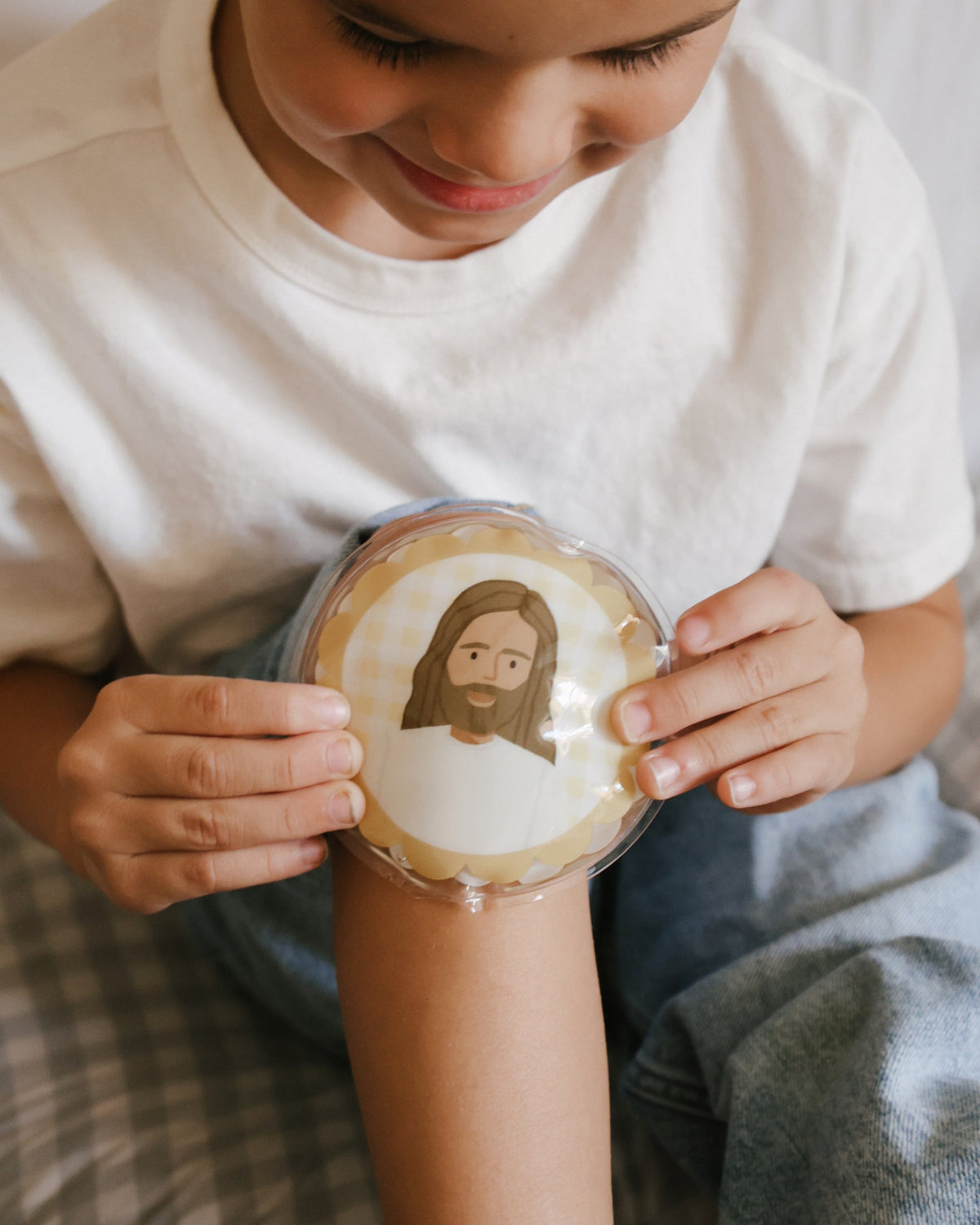 Smiling child holding a Jesus Heals reusable ice pack on a scraped knee